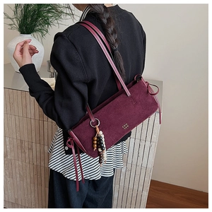 Detail of burgundy suede shoulder bag featuring gold logo and decorative beaded charms