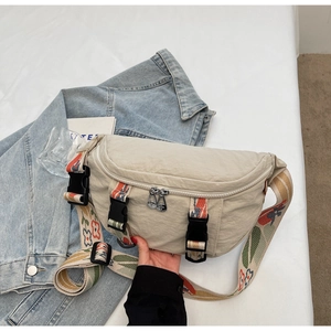 Detail of light beige canvas chest bag featuring colorful embroidered strap and dual zippers