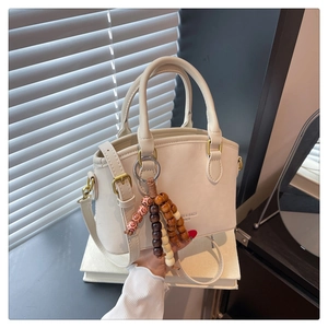 Detail of a cream faux leather trapezoid bag with beaded charm and metal feet