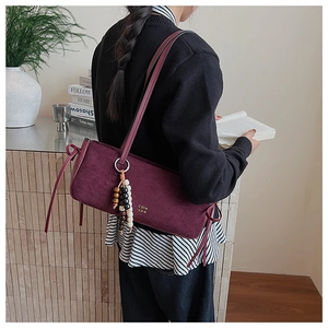Close-up of burgundy suede shoulder bag with ribbon bow and beaded tassel accessory