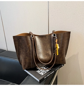 Detail of dark brown vintage faux leather tote bag with colorful beaded charm on sofa