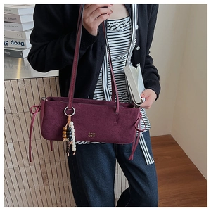Detail of burgundy suede shoulder bag featuring a gold logo and colorful tassel charm