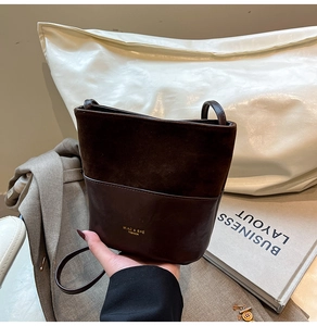 Detail of dark brown bucket bag featuring suede and leather patchwork with gold logo