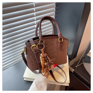Detail view of brown leopard embossed bucket bag with wooden bead charm on a book