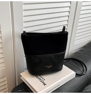 Detail of black bucket bag featuring suede and leather patchwork with gold logo branding