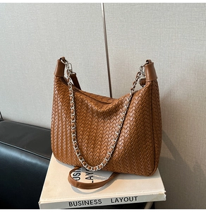 Detail of a brown woven hobo bag featuring wide straps and a chunky silver metal chain