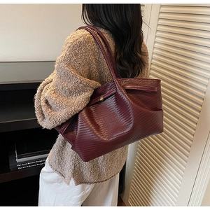 Side view of large burgundy woven tote bag with slim shoulder straps on a female model
