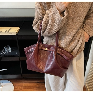 Detail of burgundy tote bag featuring woven leather texture and elegant gold buckle