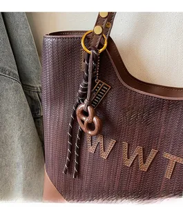 Detail of dark brown woven tote bag with leather handles and pretzel charm accessory