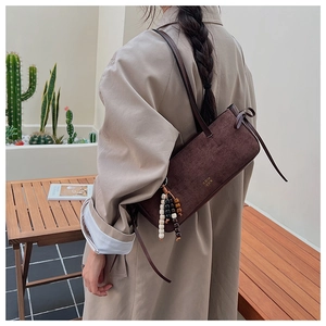 Detailed view of brown suede shoulder bag with decorative wooden beads and gold logo