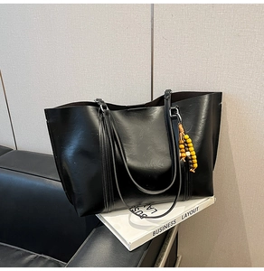 Detail of black faux leather tote bag with colorful beaded charm and slim shoulder straps