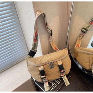 Detail of khaki crescent chest bag with colorful floral strap and buckle on a mirror
