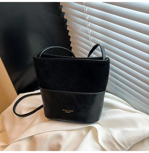 Close-up of black bucket bag featuring suede and leather patchwork with gold lettering