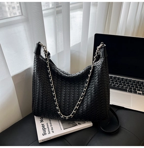 Detail of a black woven tote bag with silver chain strap on a black leather bench