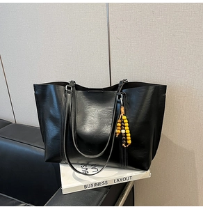 Macro detail of black faux leather tote with textured finish and wooden bead pendant