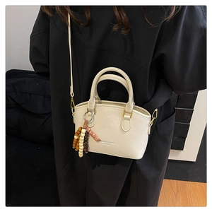 Detail view of cream white PU leather handbag with wooden bead charm and gold hardware