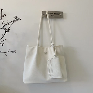 Close-up of a white leather tote bag with a metal logo and a hanging square pouch charm