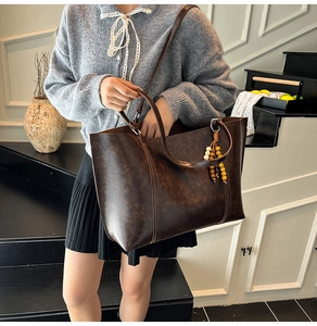 Retro large brown leather tote bag with tassel worn on shoulder in a minimalist indoor set