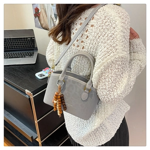 Close-up of a grey shell-shaped handbag with wood bead charm and golden lettering