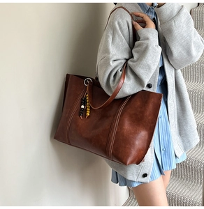 Close-up of brown tote bag featuring vertical stitching and a beaded wood charm detail