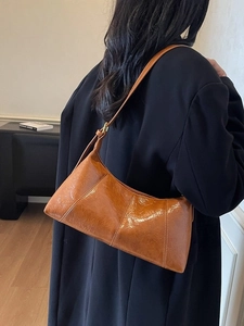 Sac baguette vintage en cuir marron brillant porté à l'épaule avec bandoulière réglable