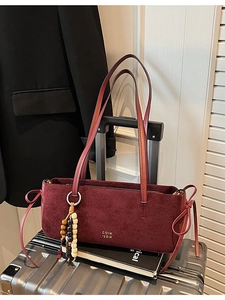 Burgundy suede shoulder bag with beaded charm displayed on a silver suitcase