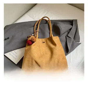Detail of mustard suede tote bag with decorative pompom and brand lettering