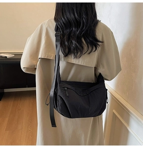 Dettaglio della borsa a tracolla in nylon nero con scomparti a zip su modella con cappotto
