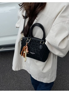 Chic black leopard embossed bucket bag with gold hardware and beaded charm on a model