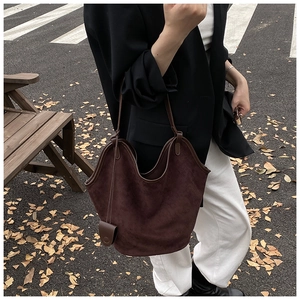 Detail of a large dark coffee suede tote bag with leather piping on an outdoor autumn street