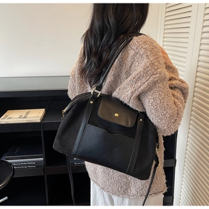 Modell trägt große matte schwarze Shopper-Tasche mit Goldschnalle im schlichten Arbeitszimmer
