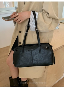 Detail of black pleated PU leather tote bag featuring a metallic logo and drawstring accents