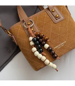 Détail d'un sac à main en daim matelassé marron avec charme en perles et logo doré