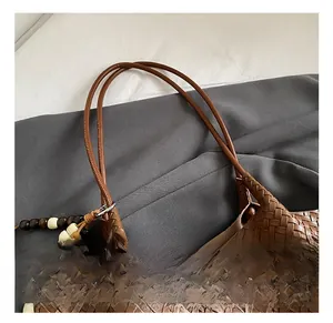 Detail of woven brown tote bag featuring comfortable handles and beaded charm accessory