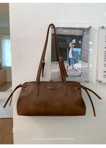 Detail of brown faux leather shoulder bag with drawstring side and metal logo plaque