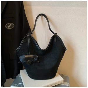 Detail of a minimalist black suede bucket bag with leather strap and glasses pouch accessory