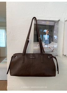 Detailed view of the dark brown leather shoulder bag featuring a metallic logo and drawstring