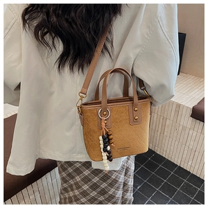 Détail du sac seau en daim marron avec motifs matelassés et breloque en perles colorées