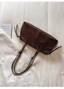 Close-up of a minimalist deep brown tote bag with metal logo and drawstring details