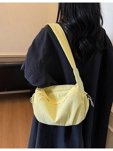 Grande borsa a tracolla in tela giallo tenue indossata da una modella in interno sobrio