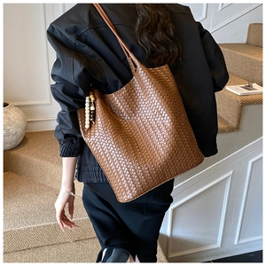 Detail of a dark brown woven tote bag with wooden bead charm worn in a retro indoor setting