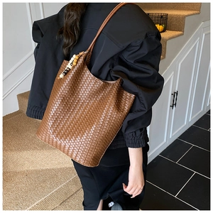 Brown woven leather tote bag featuring a decorative wooden bead charm and long shoulder strap