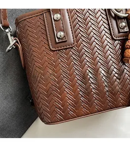 Détail d'un sac seau tressé marron avec clous métalliques et plaque de marque argentée