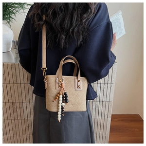 Gros plan du sac seau matelassé beige avec détails dorés et breloque décorative
