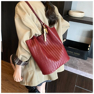 Detail of burgundy woven tote bag featuring artisan texture and decorative wooden bead