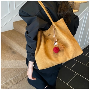 Detail of suede tote bag featuring a decorative plush pompom and embossed logo detail