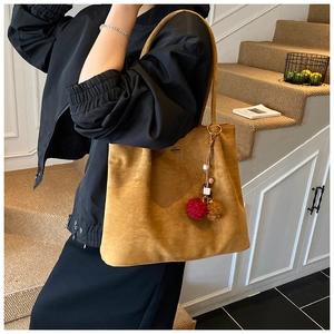 Close-up of suede tote bag with decorative pompom charms and metallic ring detail