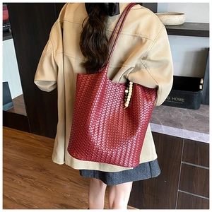 Detail of a dark red woven tote bag featuring a wooden bead charm and crossbody strap