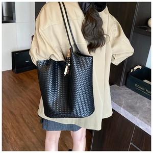 Detailed back view of a black woven tote bag with bead tassel on a model's shoulder