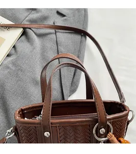 Détail de texture tressée, fermeture éclair argentée et gland à perles sur sac marron